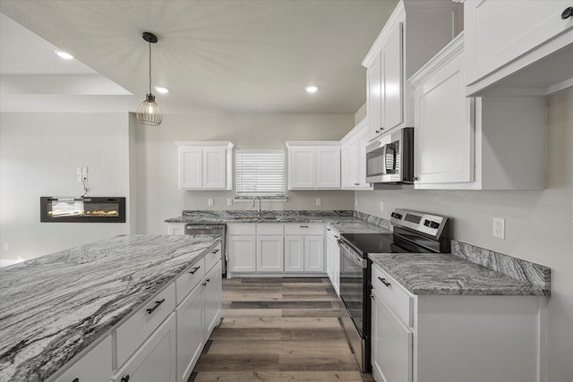 kitchen with sink, hardwood / wood-style flooring, appliances with stainless steel finishes, light stone counters, and white cabinets