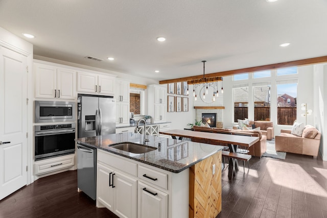 kitchen featuring appliances with stainless steel finishes, white cabinetry, sink, dark stone counters, and a center island with sink