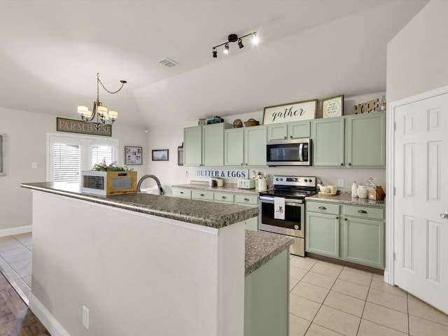 kitchen featuring lofted ceiling, stainless steel appliances, an island with sink, light tile patterned flooring, and decorative light fixtures