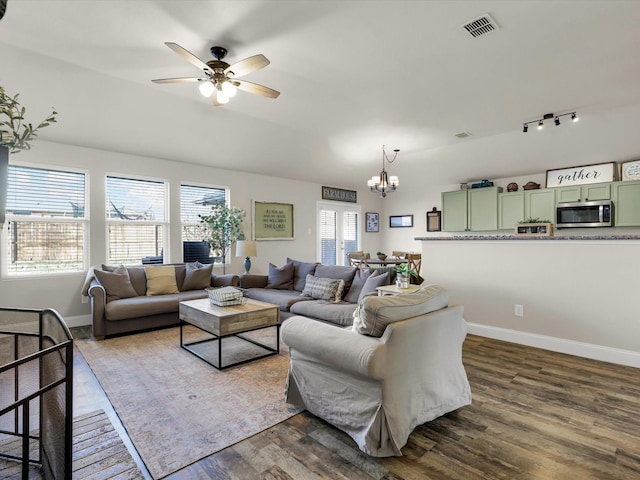 living room with ceiling fan with notable chandelier, a wealth of natural light, and dark hardwood / wood-style flooring