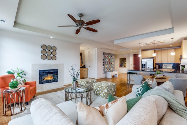 living room featuring a tray ceiling, a tiled fireplace, and light wood-type flooring