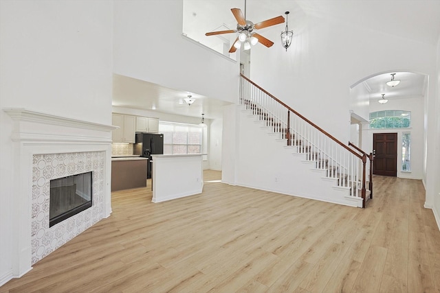 unfurnished living room with a high ceiling, stairway, a tiled fireplace, and light wood-style flooring