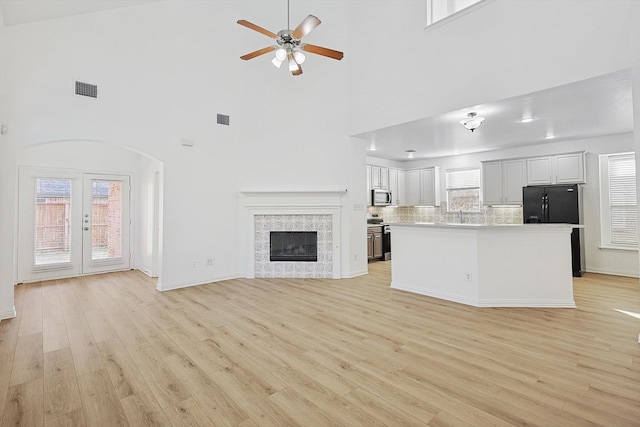 unfurnished living room with high vaulted ceiling, sink, a tiled fireplace, ceiling fan, and light hardwood / wood-style floors