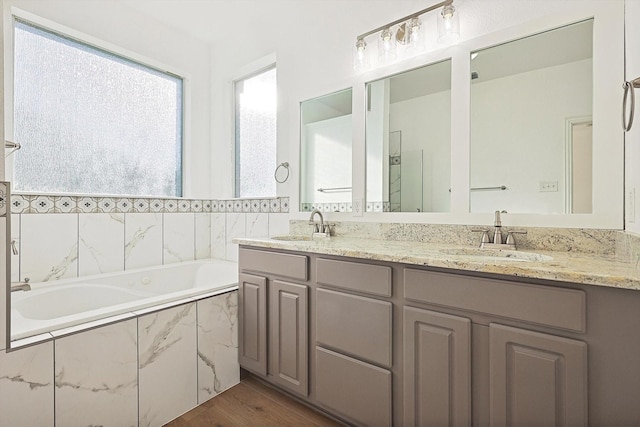 bathroom with a relaxing tiled tub, wood-type flooring, and vanity