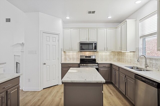 kitchen featuring appliances with stainless steel finishes, sink, white cabinets, a center island, and light hardwood / wood-style flooring