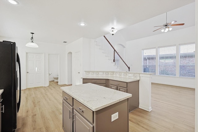 kitchen featuring light stone counters, a center island, hanging light fixtures, light wood-type flooring, and black refrigerator