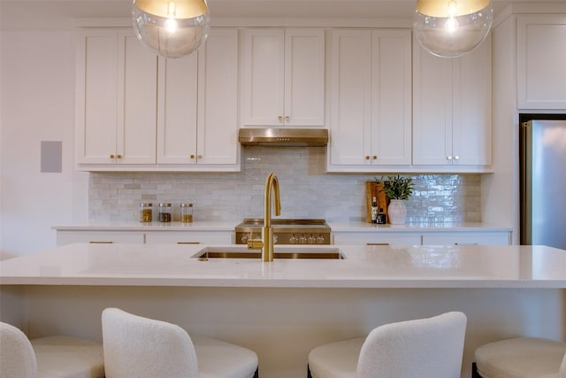 kitchen featuring tasteful backsplash, a kitchen island with sink, white cabinets, and stainless steel refrigerator