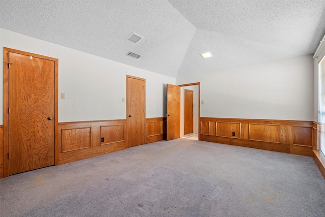 carpeted empty room featuring vaulted ceiling and a textured ceiling