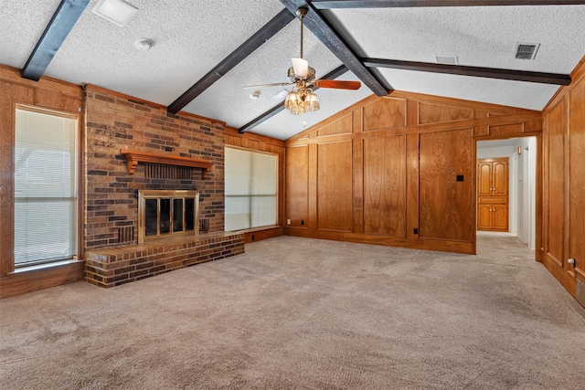 unfurnished living room featuring wood walls, vaulted ceiling with beams, light colored carpet, a brick fireplace, and a textured ceiling