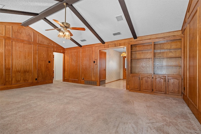 unfurnished living room with vaulted ceiling with beams, wooden walls, light colored carpet, and a textured ceiling