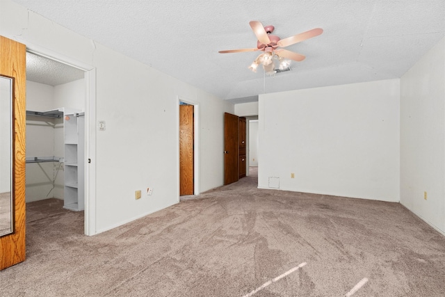 unfurnished bedroom with ceiling fan, carpet, a textured ceiling, a walk in closet, and a closet