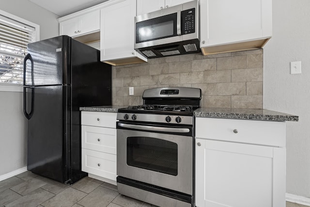 kitchen featuring appliances with stainless steel finishes, white cabinetry, tile patterned flooring, tasteful backsplash, and dark stone counters