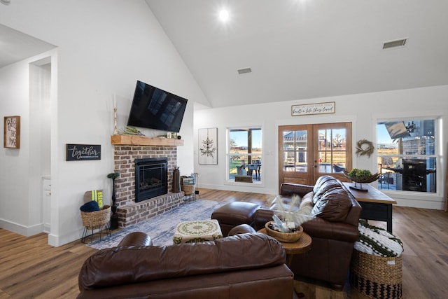 living room with a brick fireplace, wood-type flooring, high vaulted ceiling, and french doors