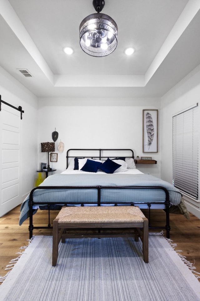 bedroom with hardwood / wood-style floors, a barn door, and a raised ceiling