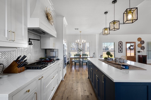 kitchen featuring white cabinetry, decorative light fixtures, blue cabinetry, and custom range hood