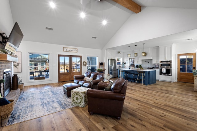 living room featuring french doors, high vaulted ceiling, light hardwood / wood-style flooring, beamed ceiling, and a fireplace