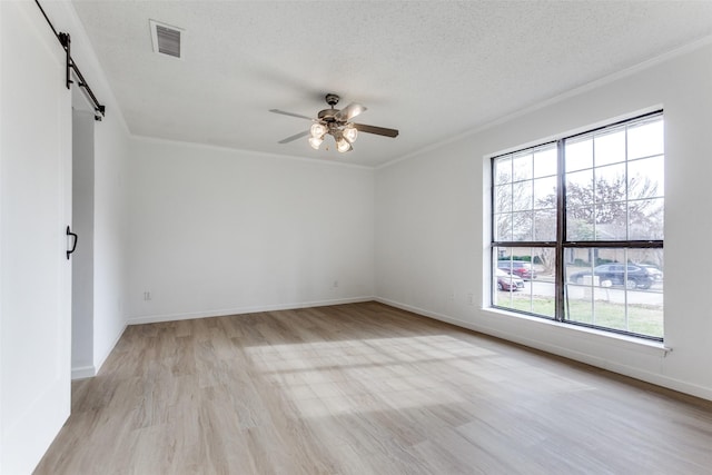 spare room featuring crown molding, ceiling fan, light hardwood / wood-style floors, a textured ceiling, and a barn door