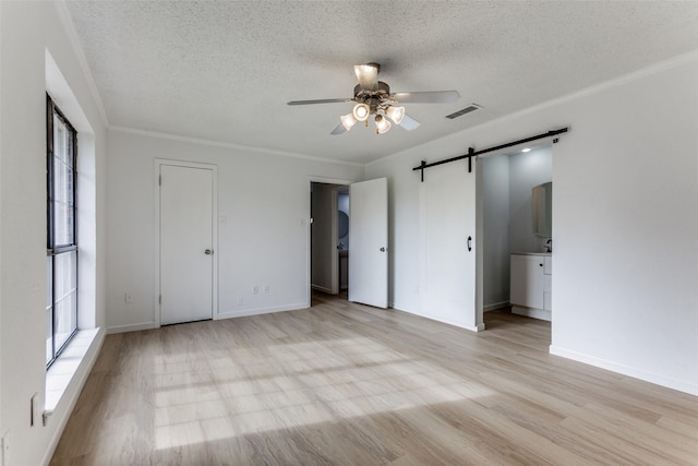 unfurnished bedroom featuring ensuite bathroom, a textured ceiling, light hardwood / wood-style flooring, ceiling fan, and a barn door