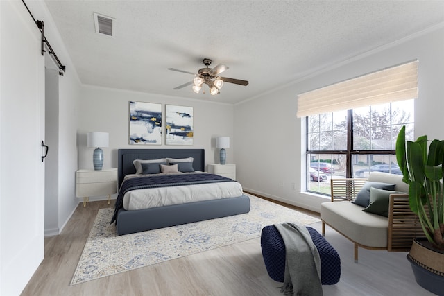 bedroom featuring a barn door, a textured ceiling, ceiling fan, and light hardwood / wood-style floors