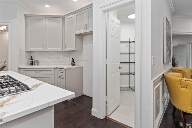 kitchen with gray cabinetry, decorative backsplash, ornamental molding, light stone countertops, and dark wood-type flooring