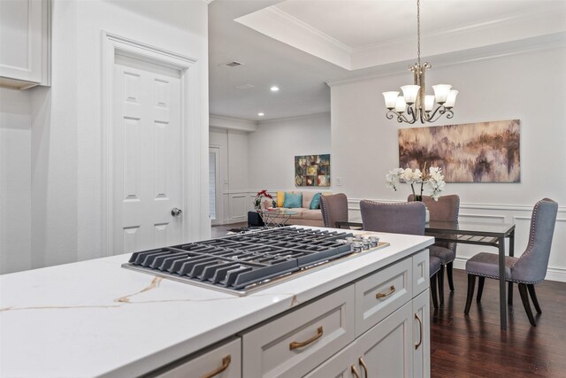 kitchen with stainless steel gas cooktop, crown molding, decorative light fixtures, a raised ceiling, and light stone countertops