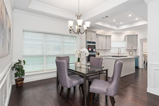 dining area with sink, dark wood-type flooring, a notable chandelier, ornamental molding, and a raised ceiling