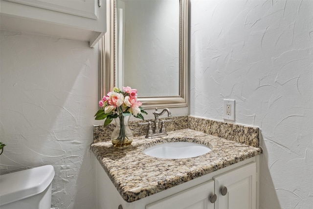 half bath featuring toilet, vanity, and a textured wall