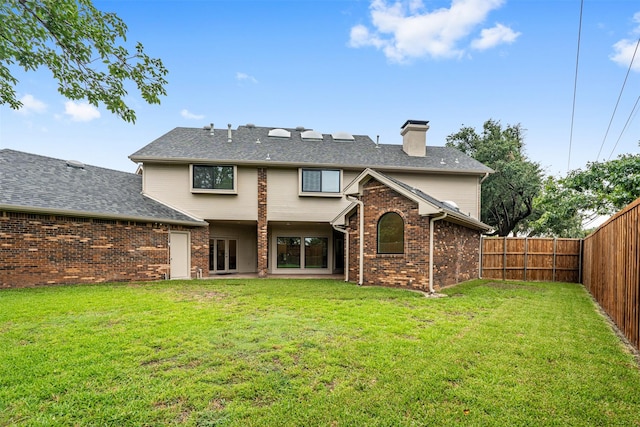 back of property featuring brick siding, a fenced backyard, a chimney, and a yard