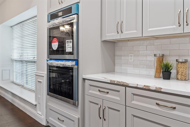 kitchen with backsplash, light stone counters, white cabinets, dark hardwood / wood-style flooring, and stainless steel double oven