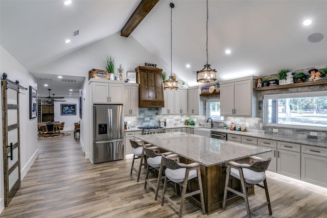 kitchen featuring appliances with stainless steel finishes, a center island, wood-type flooring, a kitchen bar, and decorative light fixtures