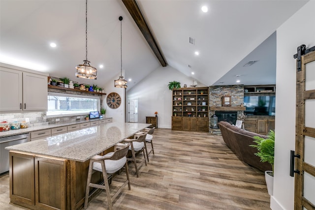 kitchen featuring a kitchen island, decorative light fixtures, backsplash, stainless steel dishwasher, and a barn door