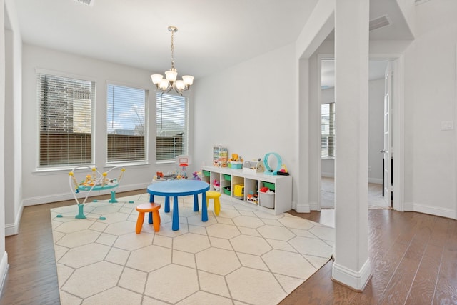 game room featuring an inviting chandelier, a healthy amount of sunlight, and light wood-type flooring