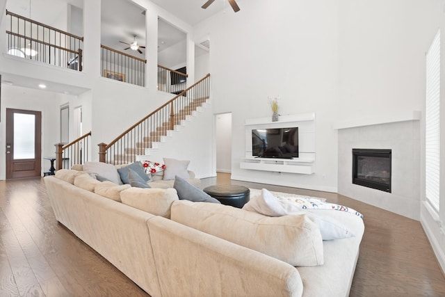 living room with dark hardwood / wood-style flooring, a tiled fireplace, ceiling fan, and a high ceiling