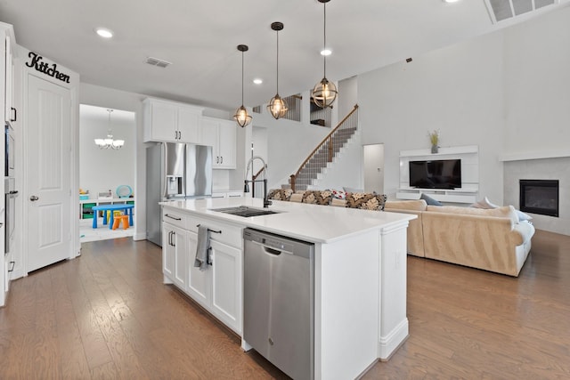 kitchen with sink, appliances with stainless steel finishes, an island with sink, white cabinets, and decorative light fixtures