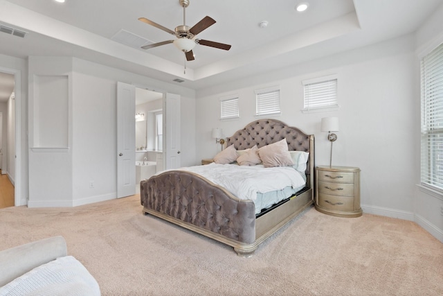 bedroom featuring connected bathroom, a tray ceiling, carpet floors, and ceiling fan