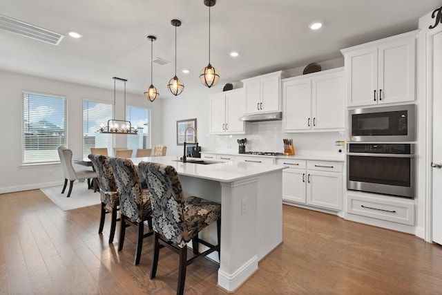 kitchen featuring sink, decorative light fixtures, a center island with sink, appliances with stainless steel finishes, and white cabinets