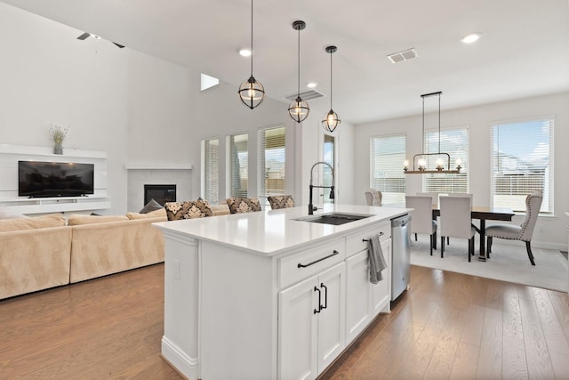 kitchen with sink, dishwasher, white cabinetry, an island with sink, and decorative light fixtures