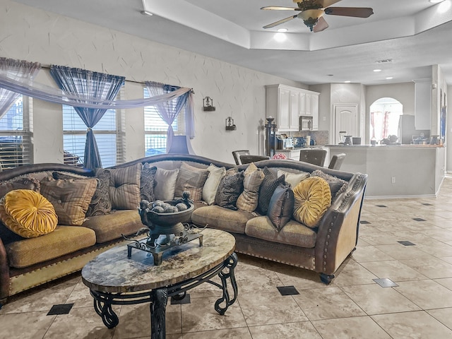 tiled living room featuring ceiling fan and a tray ceiling