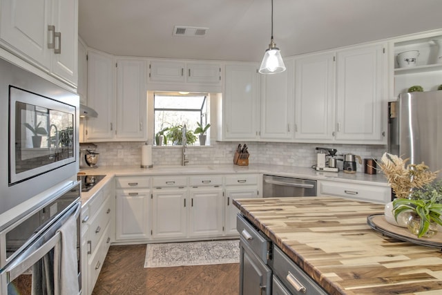 kitchen featuring white cabinetry, stainless steel appliances, decorative light fixtures, and butcher block countertops