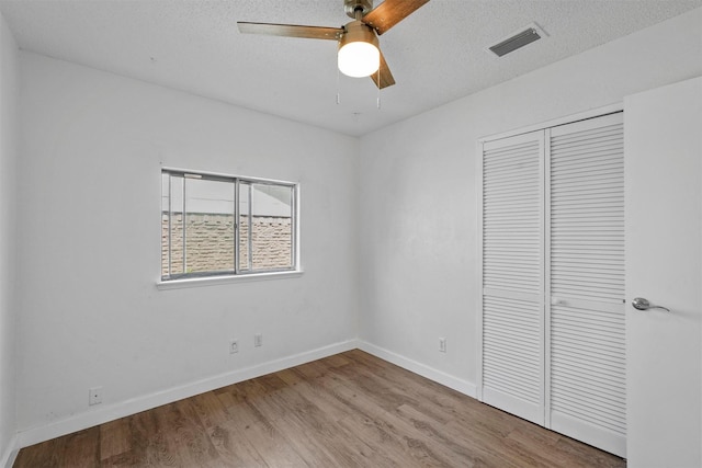 unfurnished bedroom featuring light hardwood / wood-style flooring, a textured ceiling, ceiling fan, and a closet