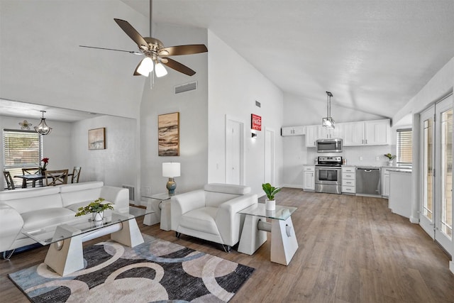 living room with ceiling fan with notable chandelier, high vaulted ceiling, and light wood-type flooring