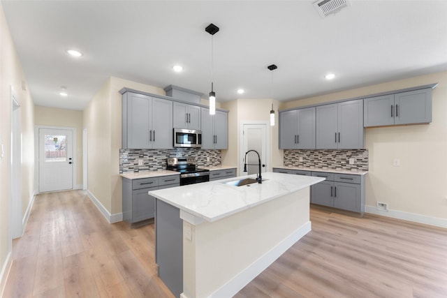 kitchen featuring pendant lighting, sink, appliances with stainless steel finishes, light stone counters, and an island with sink