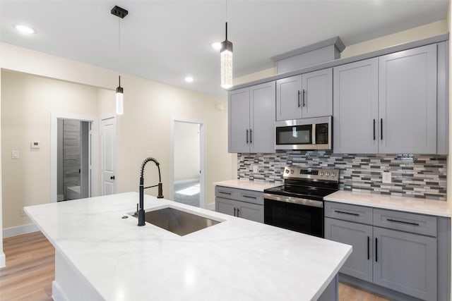 kitchen featuring sink, a kitchen island with sink, hanging light fixtures, stainless steel appliances, and light stone countertops