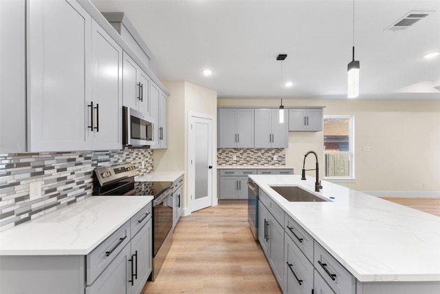 kitchen with pendant lighting, sink, stainless steel appliances, light stone countertops, and a center island with sink