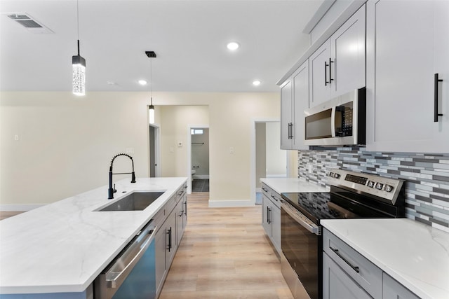 kitchen featuring sink, appliances with stainless steel finishes, backsplash, an island with sink, and decorative light fixtures