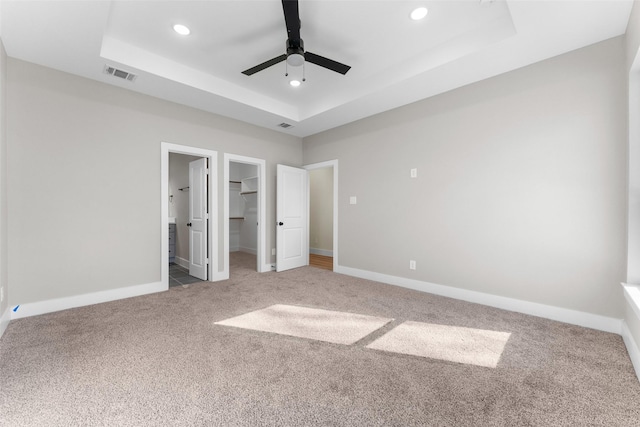 unfurnished bedroom featuring ceiling fan, carpet flooring, connected bathroom, a tray ceiling, and a walk in closet