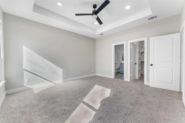 unfurnished bedroom with ceiling fan, a walk in closet, connected bathroom, and a raised ceiling