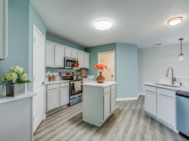 kitchen featuring sink, appliances with stainless steel finishes, white cabinetry, a kitchen island, and decorative light fixtures