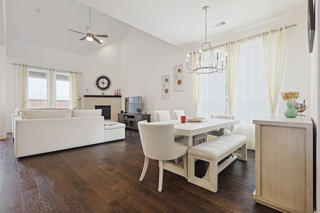 dining space featuring high vaulted ceiling, ceiling fan with notable chandelier, a fireplace, and dark hardwood / wood-style flooring