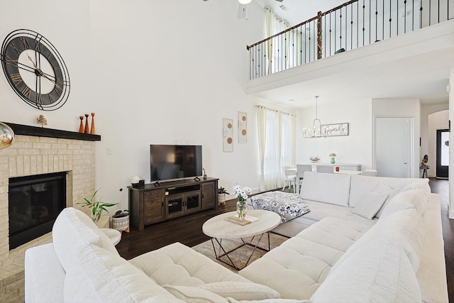 living room featuring ceiling fan with notable chandelier, hardwood / wood-style floors, a brick fireplace, and a high ceiling